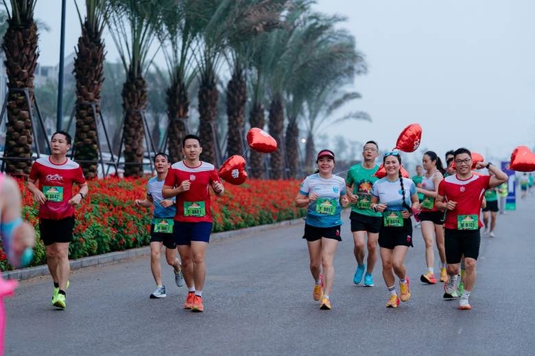 A group of people running on a road with flowers and trees Description automatically generated
